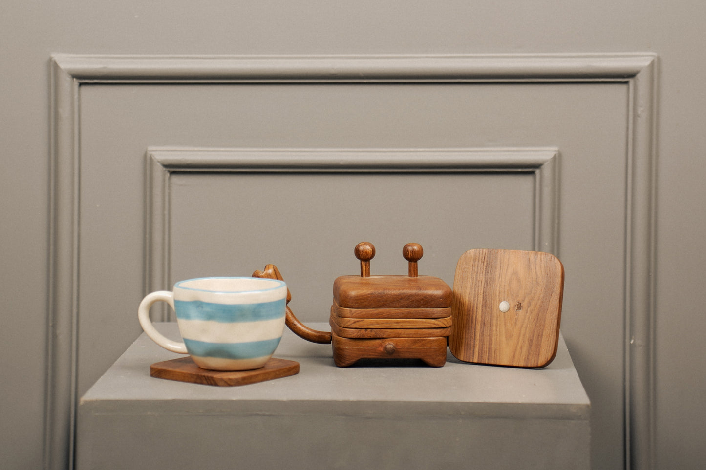 Wooden toaster, striped mug, and wooden cutting board on a gray surface with a neutral background