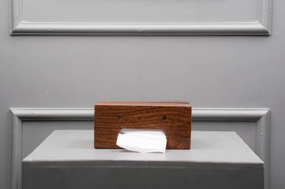 Wooden tissue box with a white tissue on a gray surface against a gray wall.