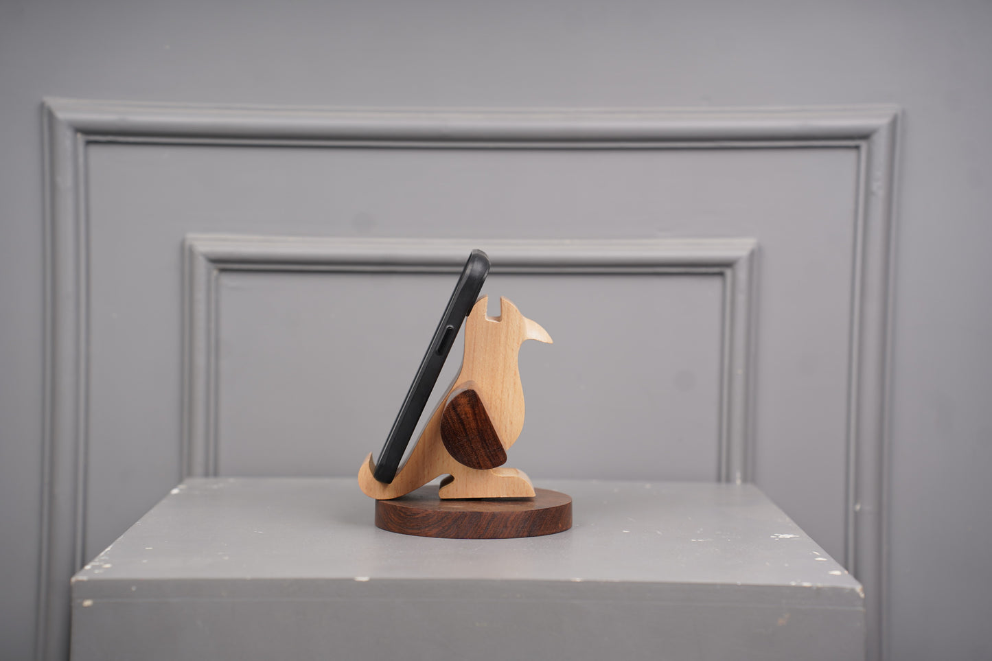 Wooden phone stand holding a smartphone on a gray surface with a gray background