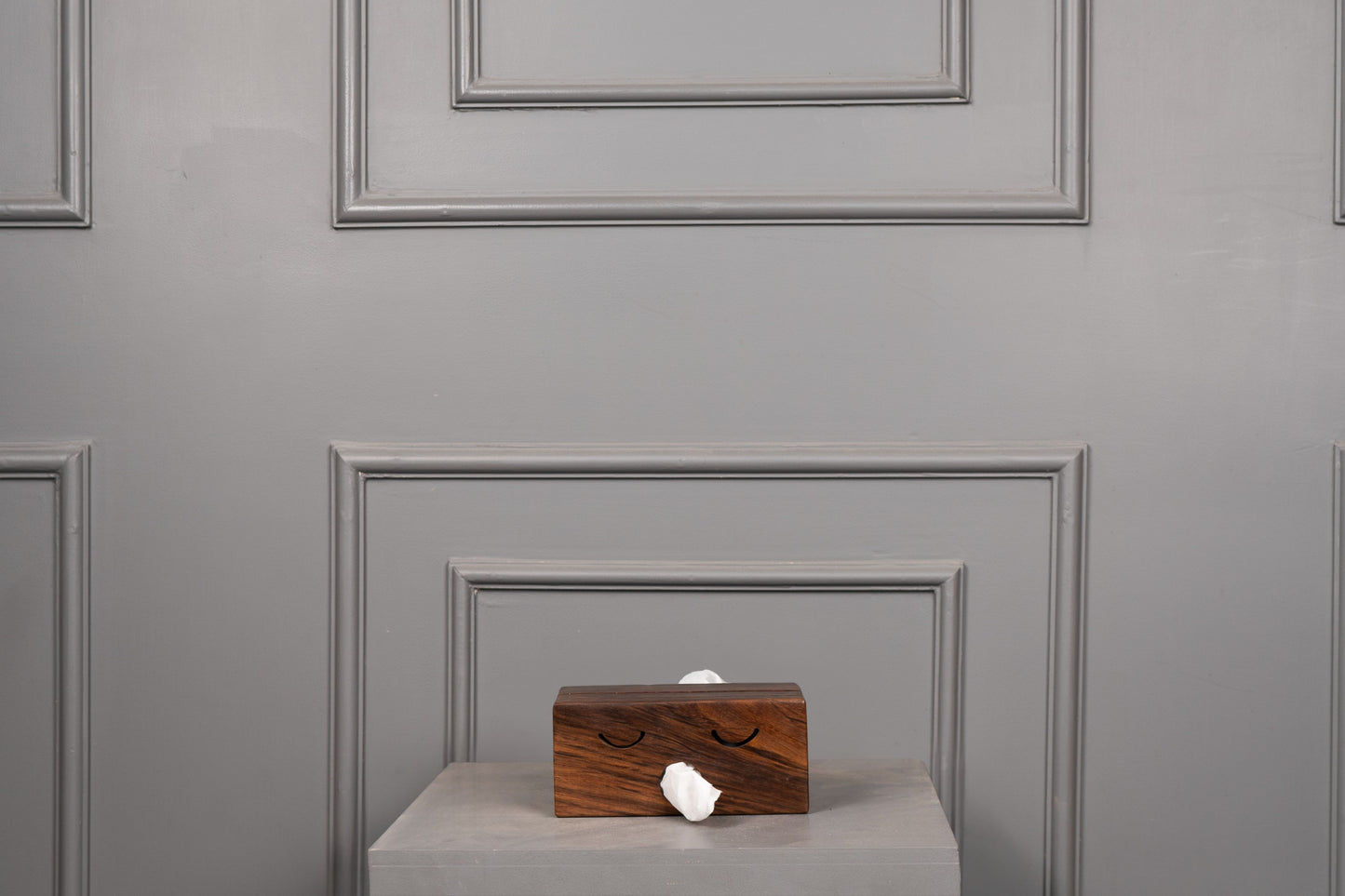 Wooden box with a white object on a gray surface against a gray paneled wall